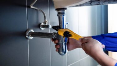 Plumber fixing white sink pipe with adjustable wrench.